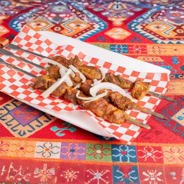 Four skewers of grilled meat with sliced onions on a white tray with red checkered paper.