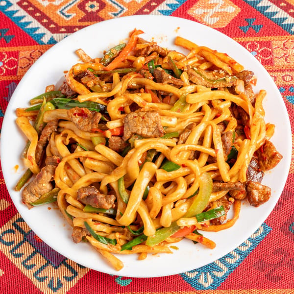 A white plate filled with stir-fried noodles, beef, and vegetables on a colorful patterned tablecloth.