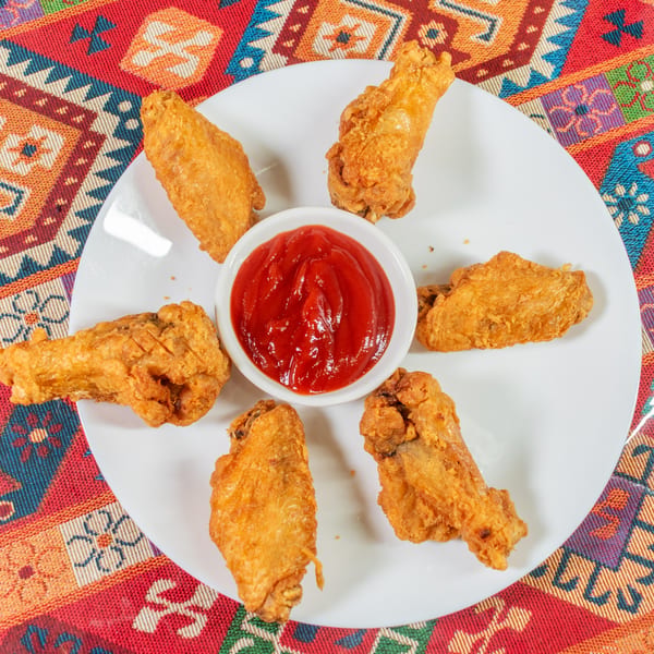 Golden-brown fried chicken wings arranged around a small bowl of red ketchup on a white plate.