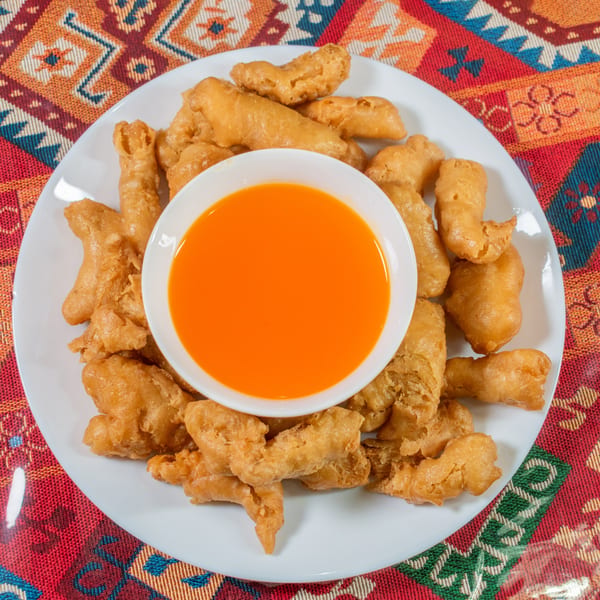 Crispy fried chicken pieces on a white plate with a small bowl of orange dipping sauce.