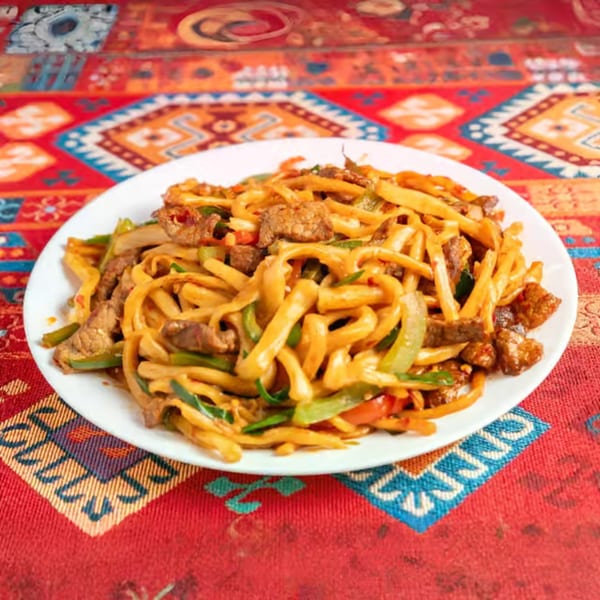 A white plate filled with stir-fried noodles, beef, and vegetables on a colorful patterned tablecloth.