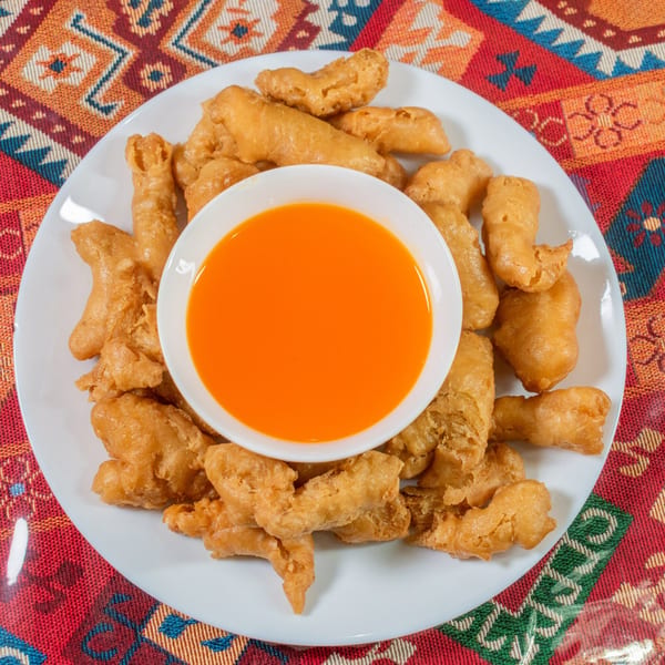 Crispy fried chicken pieces on a white plate with a side of orange dipping sauce.
