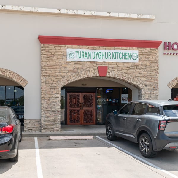Exterior of Turan Uyghur Kitchen, a restaurant with a stone facade and carved wooden doors.