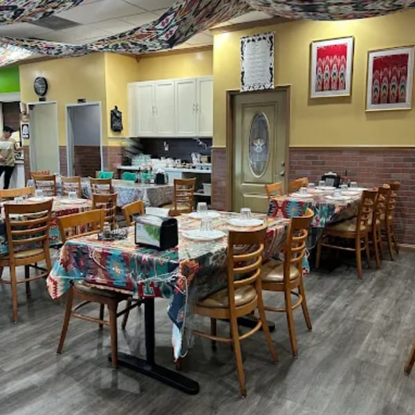 Interior of Turan Uyghur Kitchen with patterned tablecloths, wooden chairs, and yellow walls.
