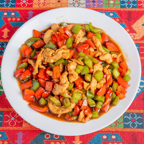Chicken stir-fry with red and green bell peppers in a savory sauce on a white plate.