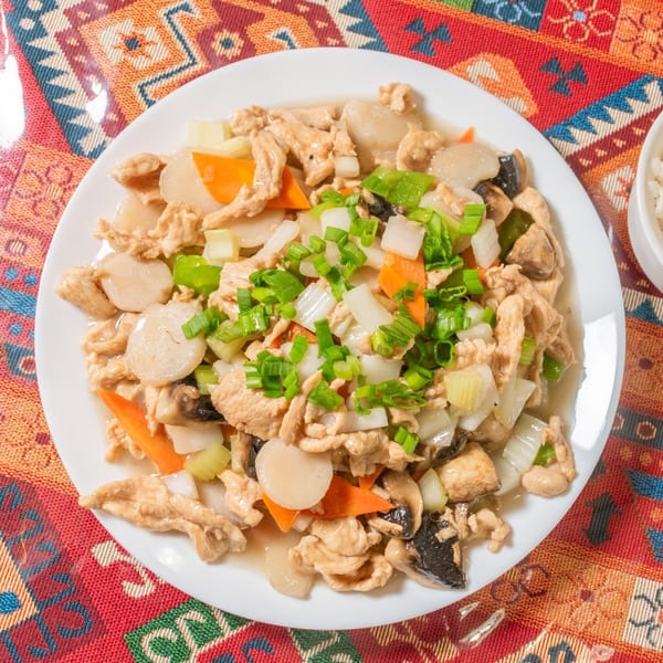 Chicken and scallops stir-fry with vegetables, including carrots, onions, and mushrooms, on a white plate.