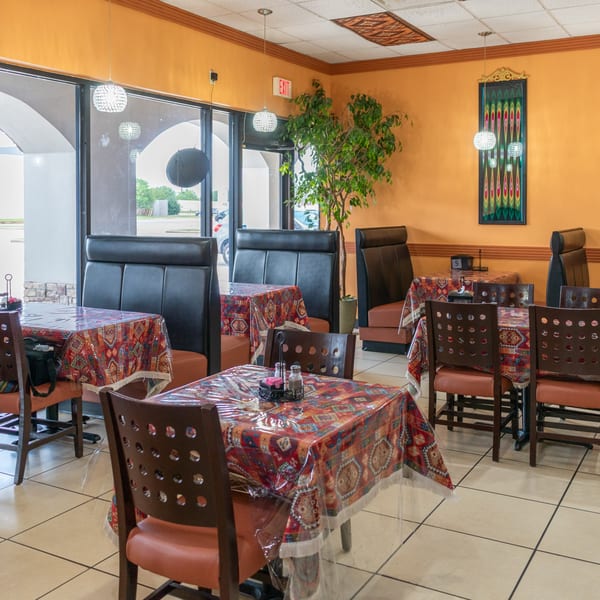 Restaurant interior with orange walls, patterned tablecloths, black booths, and wooden chairs.