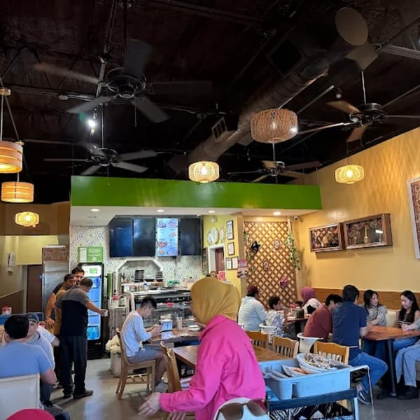 Diners seated at wooden tables in a brightly lit Turan Uyghur Kitchen restaurant with ceiling fans.