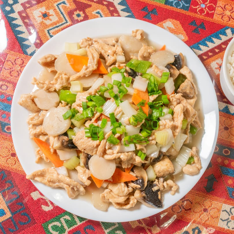Chicken with vegetables, including carrots, onions, and scallions, on a white plate.