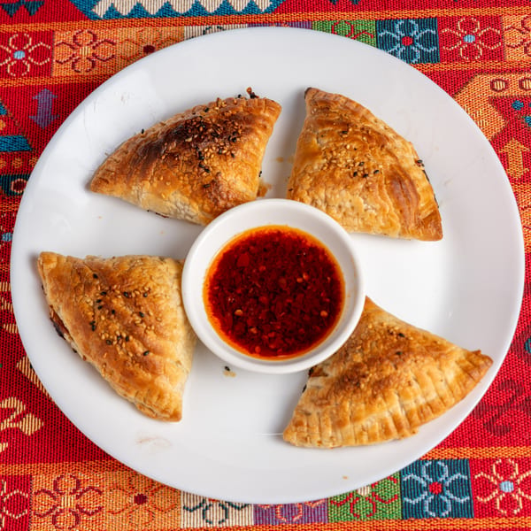 Four golden-brown pastries with sesame seeds surround a small bowl of red chili oil on a white plate.