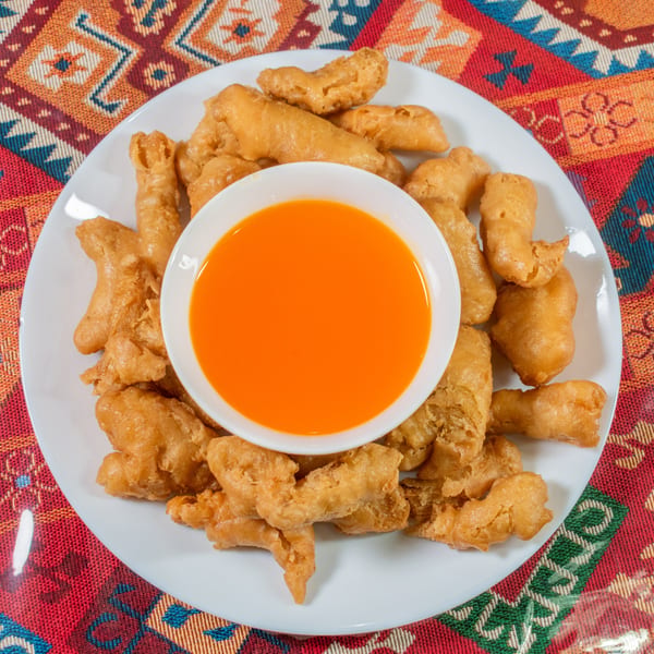 Crispy fried chicken pieces on a white plate with a small bowl of orange dipping sauce.