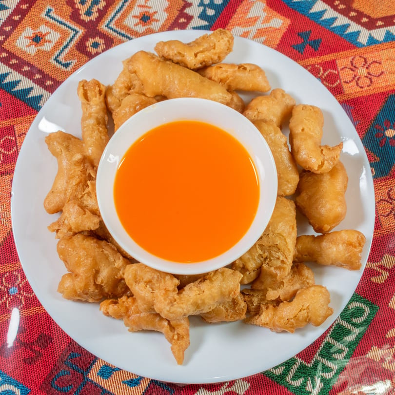Crispy fried chicken pieces with a side of bright orange sweet and sour sauce on a white plate.