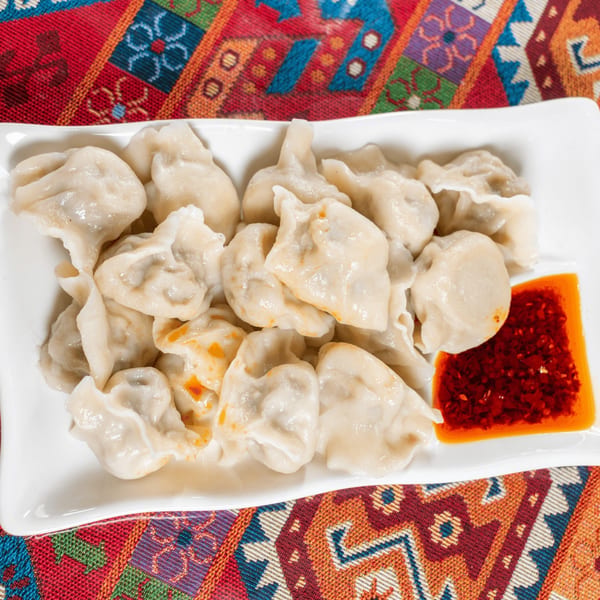 A white rectangular plate filled with steamed dumplings and a side of red chili oil.