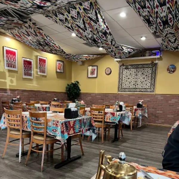 Interior of Turan Uyghur Kitchen with patterned tablecloths, yellow walls, and brick accents.