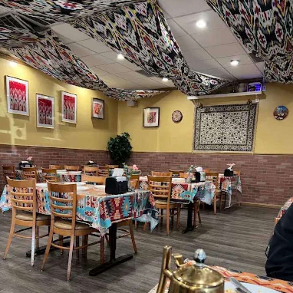 Interior of Turan Uyghur Kitchen with patterned tablecloths, yellow walls, and brick accents.